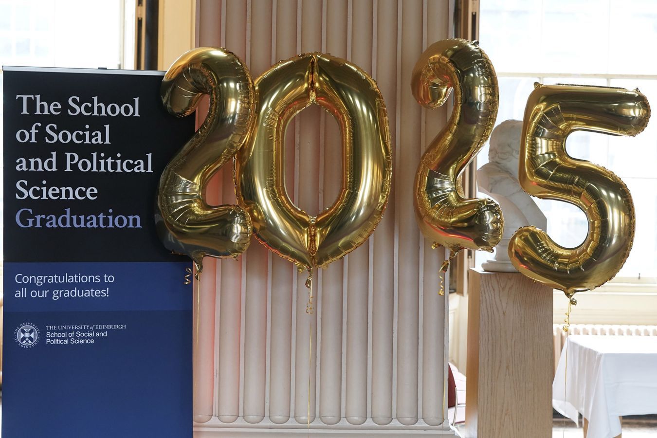 A banner reads 'The school of Social and Political Science Graduation'. Next to it are 4 balloons in the shape of the number 2025