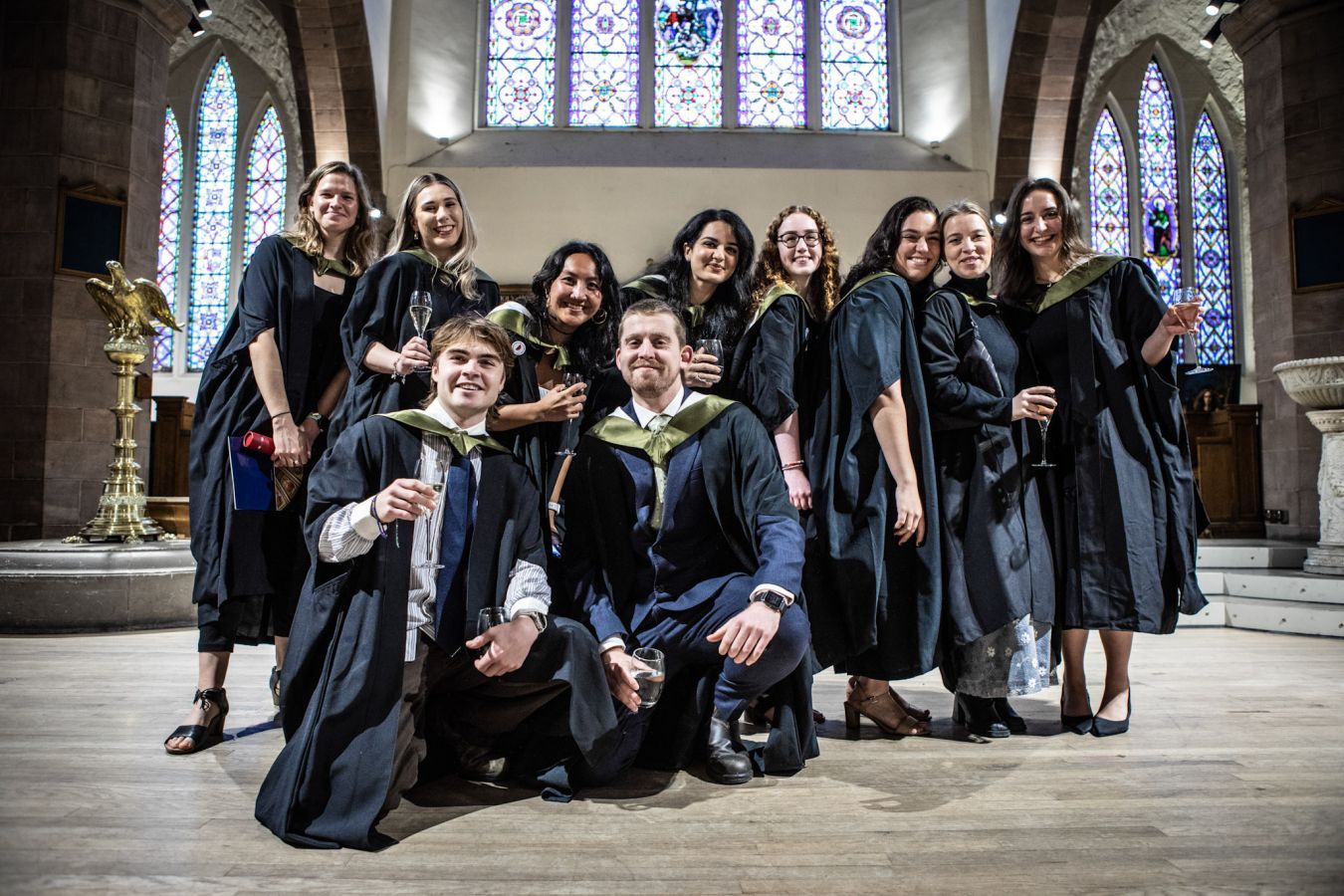 A photo of 10 graduates wearing gowns and smiling into the camera