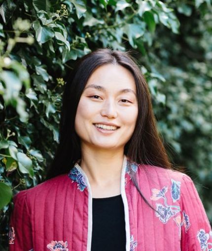 A Chinese-American woman in a red jacket standing in front of a wall of ivy