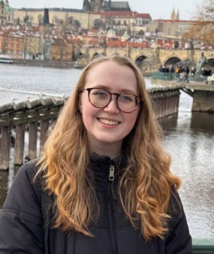 A smiling woman with long blonde hair, in front of a city landscape