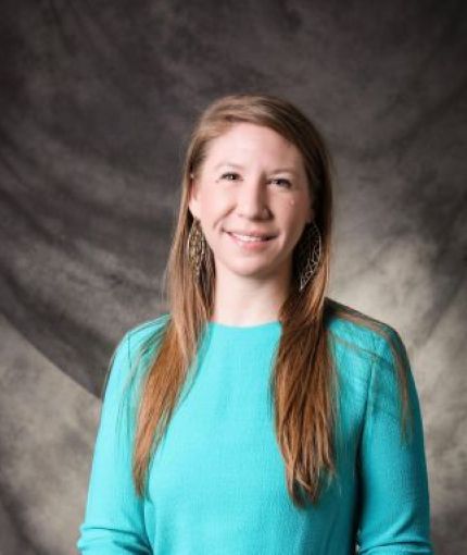 Female with long hair wearing a teal dress and gold earrings.