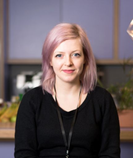 image of Sophie with purple hair wearing a black jumper and a purple background
