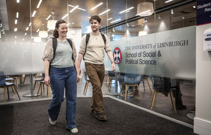 Two students walking in a building, beside a sign for the 'School of Social and Political Science'