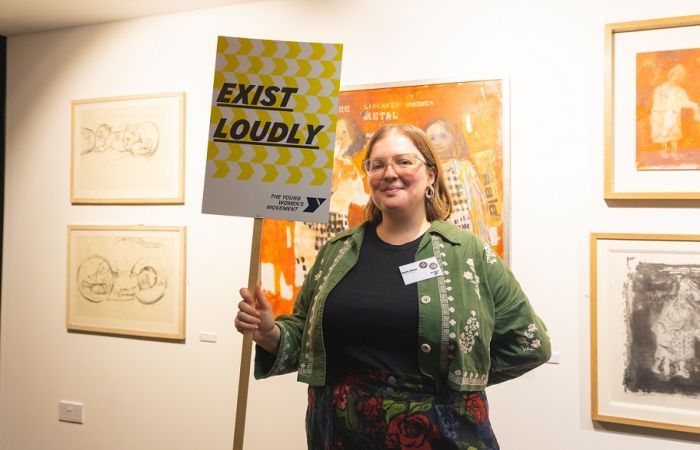Emily Mann holding up a sign that reads 'exist loudly'