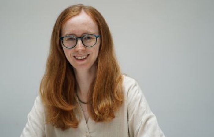 Photograph of Dr Cat Acheson, a white woman who wears glasses and has red hair.