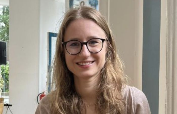 A photo of Alina, wearing a black top and beige cardigan, smiling at the camera