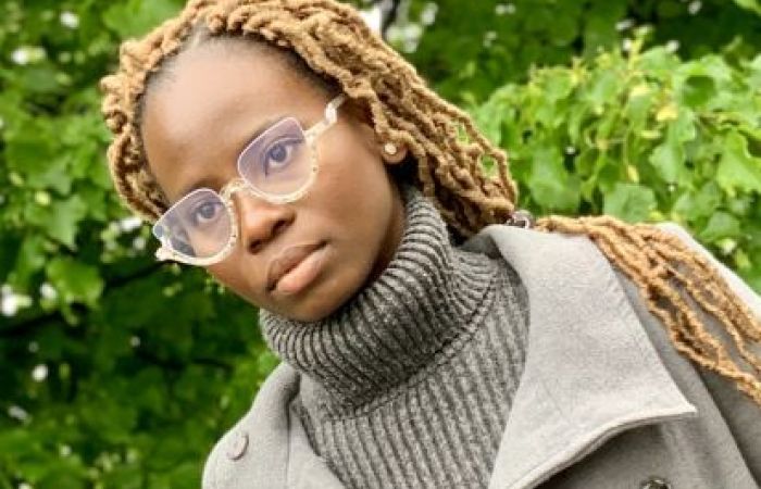 A picture of a young lady on clear frame glasses, with green trees in the background.