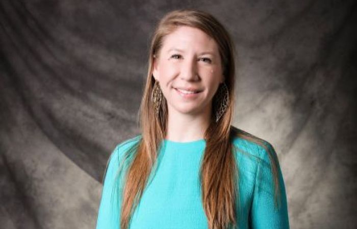 Female with long hair wearing a teal dress and gold earrings.
