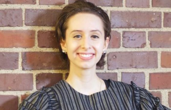 Person smiling and posing against brick wall.