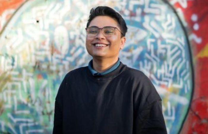 Person in black jumper, short hair, and glasses smiling into the camera
