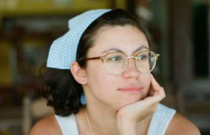A woman with short brown hair and glasses sits with her face cupped in her hand